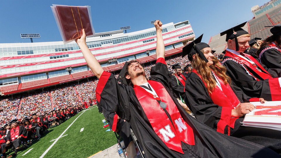 Stephen Yaghmour, a Chancellor Scholar, raises his arms in triumph with degrees in hand as he sits on the turf in Memorial Stadium during commencement in May.