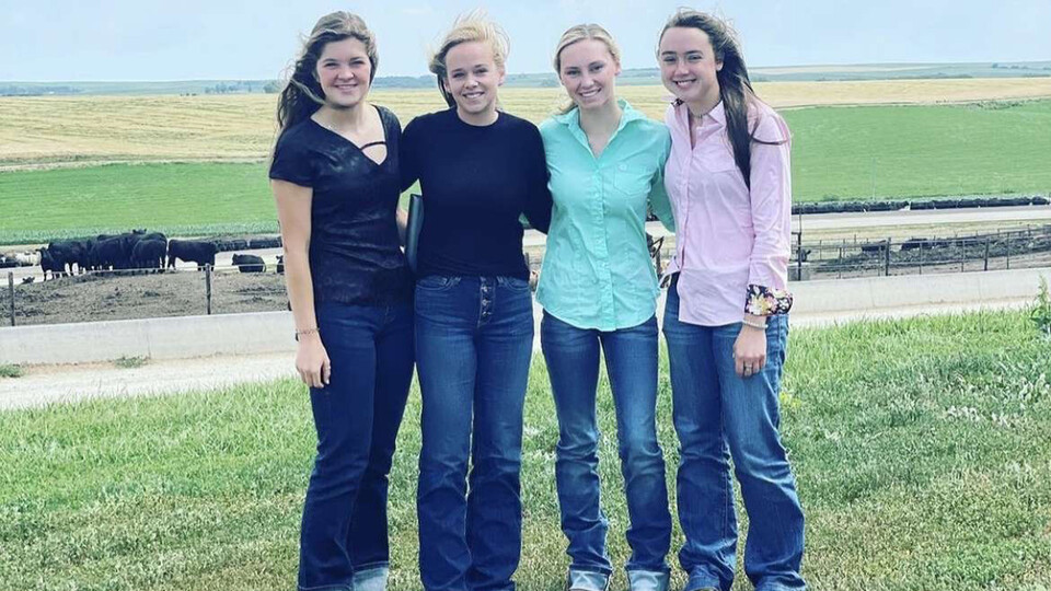 4 students standing on a hill overlooking a beef cattle operation.