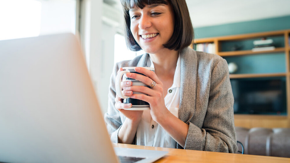 Women on laptop for virtual meeting holding coffee mug