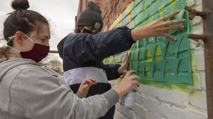 Honors students (from left) Sophie Newman and Ellie Hellman spray paint a stencil as part of the mural project in Lincoln's historic Havelock neighborhood on April 17. Students paired up to create designs for the quilt-block mural.