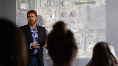 Tyler White, teaches while illuminated by a large satellite image of an Iranian oil refinery. Part of the University Honors Seminar is learning how information is obtained by such imagery.  