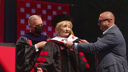 Leta Powell Drake, local television pioneer and Husker alumna, is hooded by University of Nebraska Regent Tim Clare (left) and her son, Aaron (right), during the University of Nebraska–Lincoln’s undergraduate commencement ceremony Aug. 14 at Pinnacle Bank Arena. The university presented Drake with an honorary Doctor of Humane Letters during the ceremony.