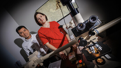 Husker scientists Hiep Vu and Sarah Sillman stand in a shadowy room, with a microscope in the foreground.