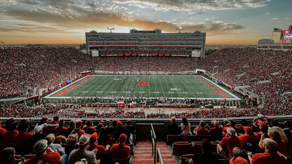 Memorial Stadium, full of fans, with colorful clouds in the background