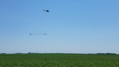 A helicopter carries a large loop of wire whose electromagnetic signaling enables extensive imagery of subsurface conditions and the creation of a 3D geological model.