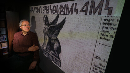 Peter Revesz poses in front of artwork of an ancient sphinx with an inscription that he deciphered.