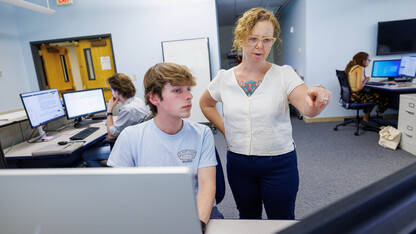 Katrina Jagodinsky stands next to a student working on a computer, with two student on computers in the background.