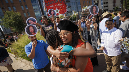 Graduate Genese Clark hugs a young woman as family and friends hold signs with the graduate's photo and a banner that reads "Congrats Dr. Clark," outside Pinnacle Bank Arena.