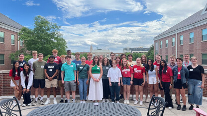 Thirty-one Husker students, all members of the Jeffrey S. Raikes School of Computer Science and Management, pose on the rooftop of the Kauffman Academic Residential Center on a partly cloudy day. The Nebraska Union and Nebraska State Capitol are visible in the background.