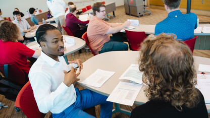 A dozen or so people converse at small tables in a classroom.