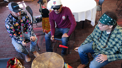 Three young men play a Native drum.