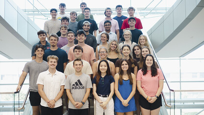 About 30 Husker students — all members of the fifth class of the Investors With Purpose program — stand on a staircase in Howard L. Hawks Hall.