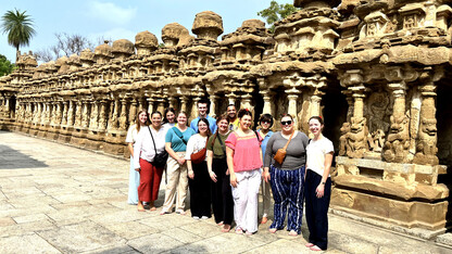 Twelve people stand outside the sandstone Kailasanathar Temple in Kanchipuram, India.