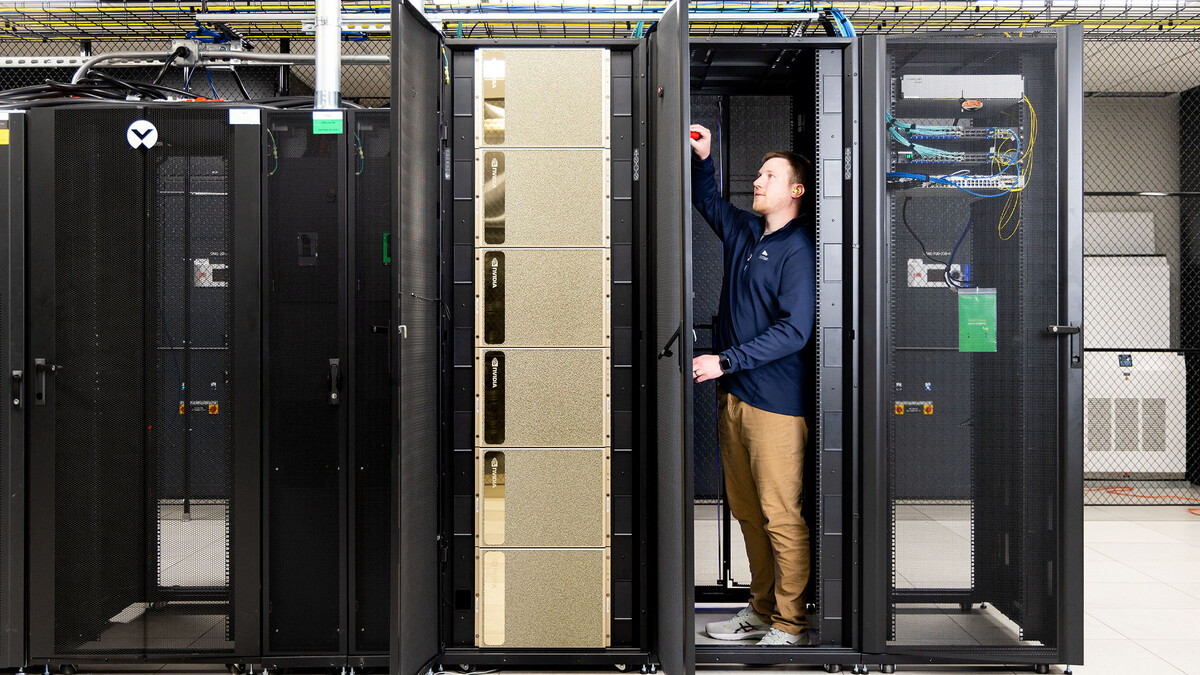A young man stands in a rack of computer equipment.