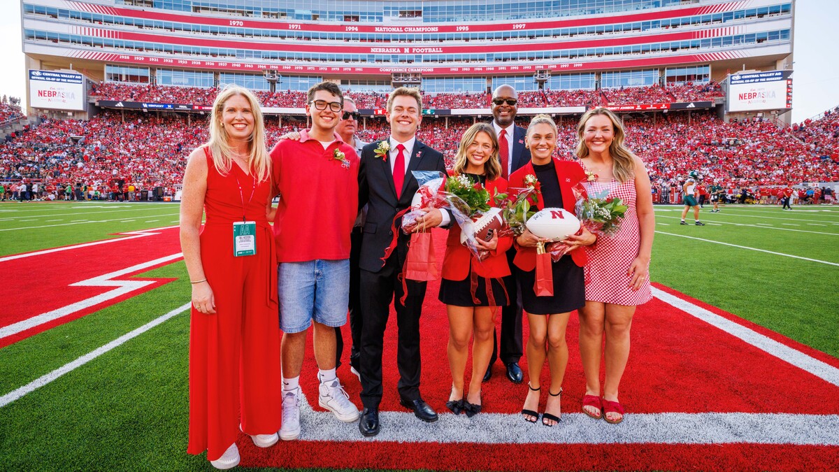 Four women and three men in red and black attire pose for a photograph at midfield in Memorial Stadium.