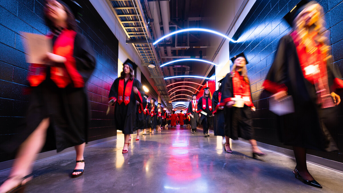 Two lines of graduates walk through a hallway in Pinnacle Bank Arena.