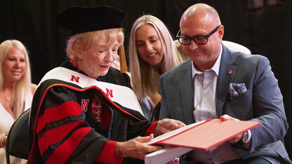 Sitting in chairs, Leta Powell Drake and two family members examine the honorary degree during the university's Aug. 14 commencement exercises in Pinnacle Bank Arena.