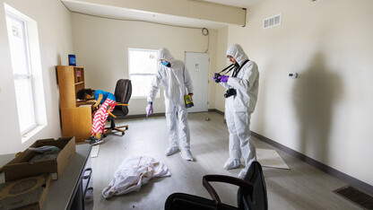 s the victim awaits the investigator’s attention, Reed Knutson points out evidence in the murder scene for Sam Thomas to photograph.