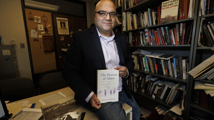 Bedross Der Matossian is photographed near his office book shelf, holding a copy of his new book, "The Horrors of Adana."