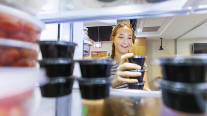 Brenna Mazour, a senior in psychology and dietetics, rearranges containers of shredded cheese in the wellness kitchen refrigerator.  The refrigerated items will be added to the kits when the meals are picked up.