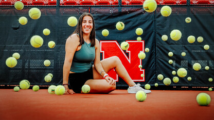 Tennis balls bounce around Isabel as she sits for a photo on the tennis court.