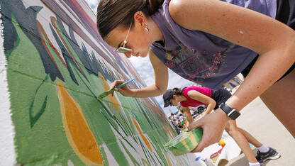 Lea Bushey, a senior in graphic design, paints stems of grass on the mural. ARTS 398 - Special Topics in Studio Art III taught by Sandra Williams. The class painted a mural at the Premier Buick, Chevrolet, and GMC dealership in Beatrice.