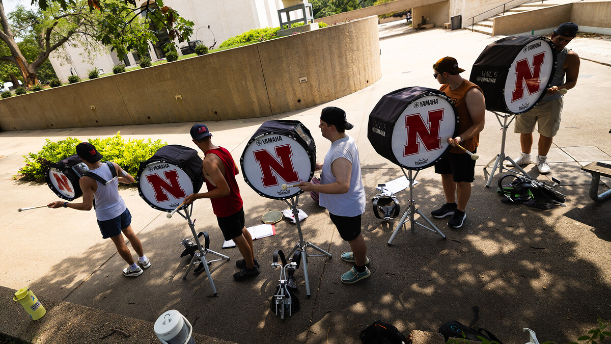 Five drummers from the Cornhusker Marching Band practicing in the shade.