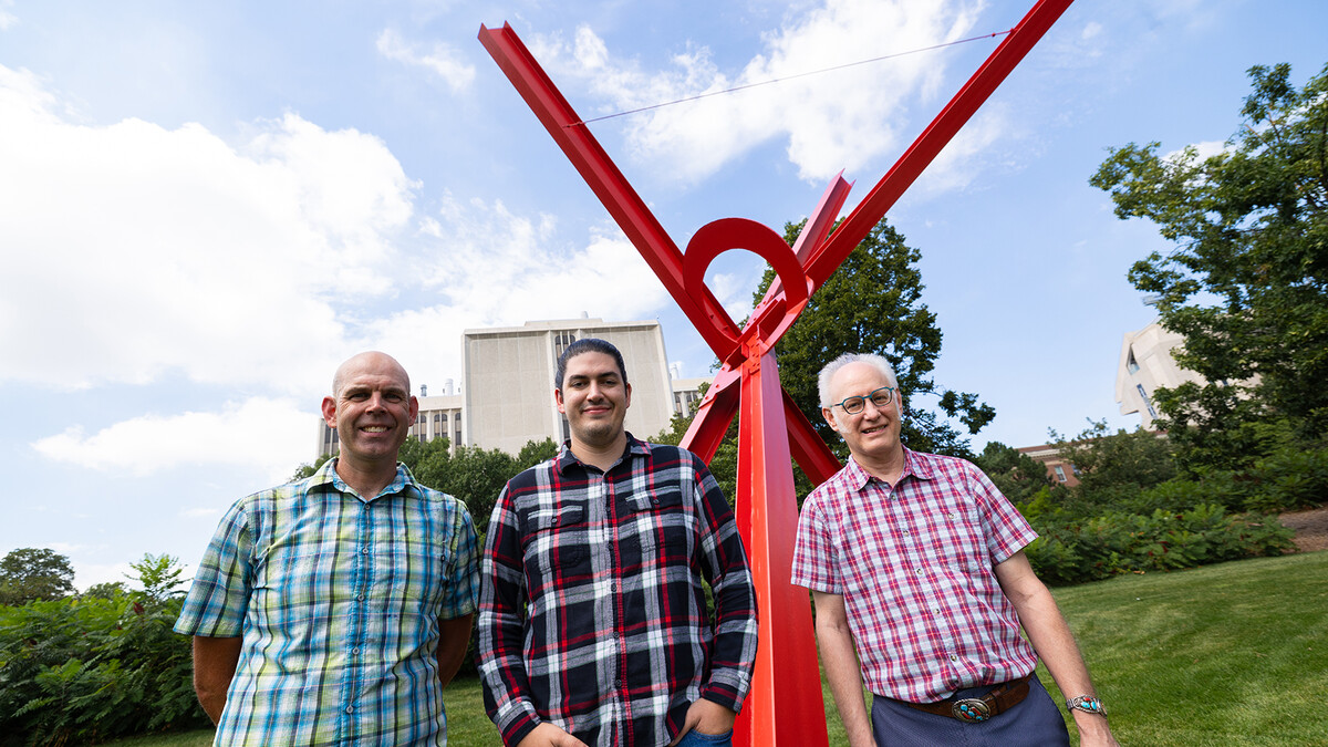 Three UNL researcher standing by the red steel beam sculpture, "Old Glory."