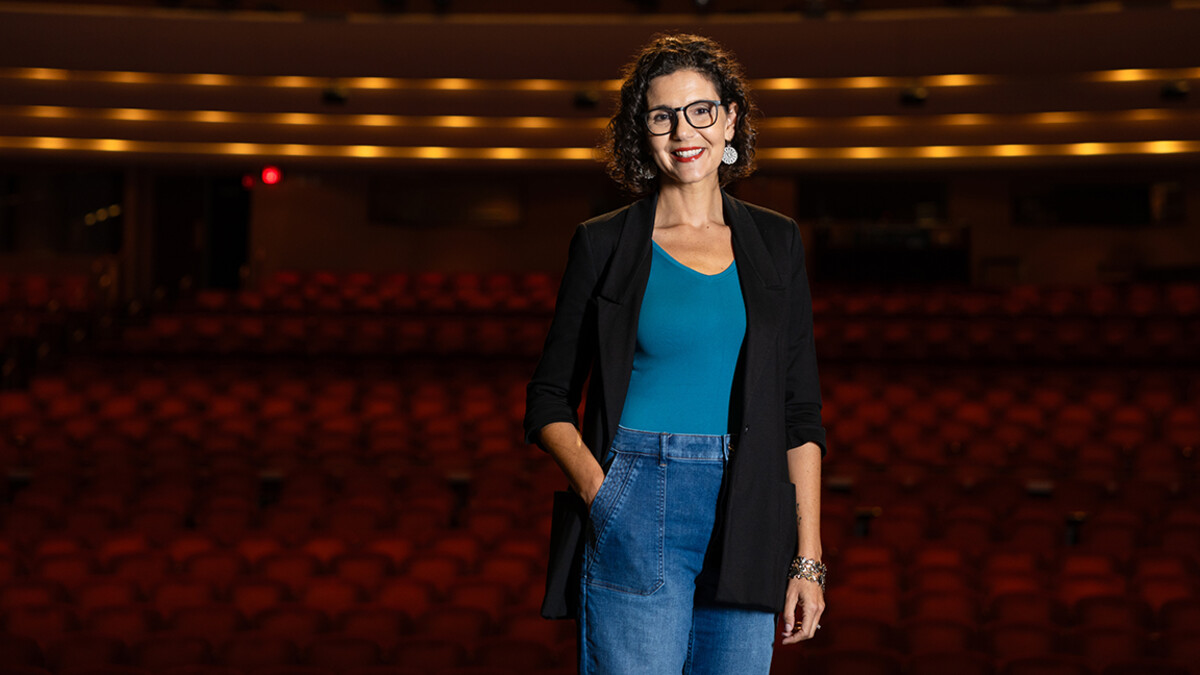 A woman stands in front of auditorium seating.