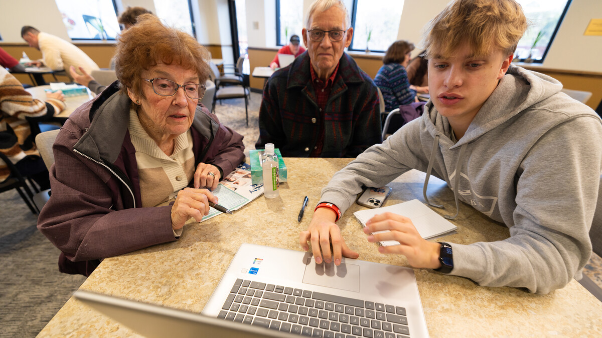 Three people sit around a table as one navigates a laptop desktop.