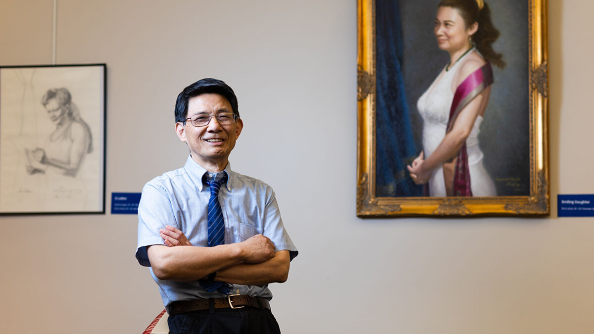 A man stands with his arms crossed in front of paintings.