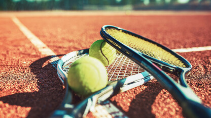 tennis rackets and two yellow tennis balls lay on a tennis court