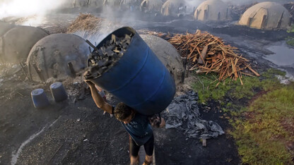 A slave carries a drum of burned wood to make charcoal in Brazil. Forests have been decimated in the country to create coal, which is then used for Brazil's steel industry. The forests are cut down and burned with slave labor.