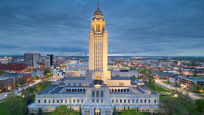 The Nebraska State Capitol stands tall and illumniated against the Lincoln, Nebraska, skyline at dusk.