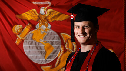 L.J. Bird in commencement regalia with U.S. Marine Corps flag in background