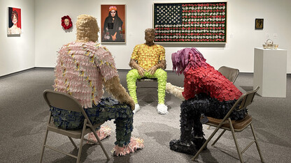 Image of the Eistentrager-Howard Gallery with items from the exhibition, including three pinatas of life-sized people sitting on metal chairs having a conversation.