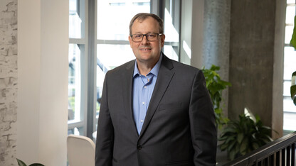 Matt Blomstedt in a suit jacket and button up shirt standing by a window.