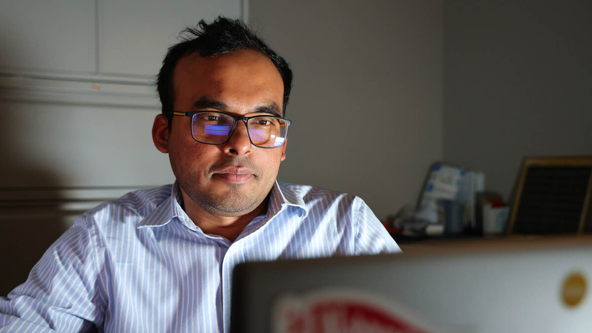 Nipuna Chamara, a brown man with short black hair and square-framed glasses, sits in a white button-up looking at a laptop screen.