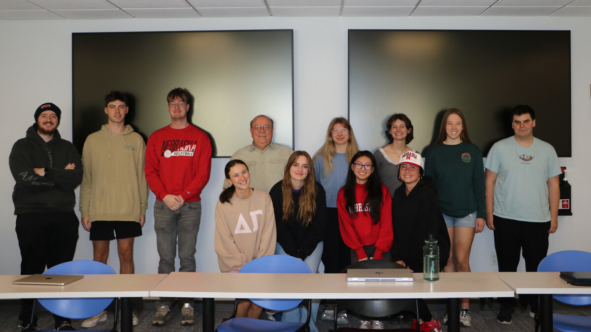 A crowd of students smile with professor Donald Beahm, a white bald man with glasses in a cream shirt.