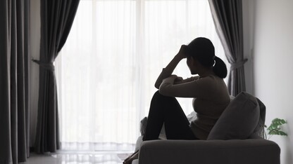 A woman in silhouette sits on a sofa and appears to be pensive.