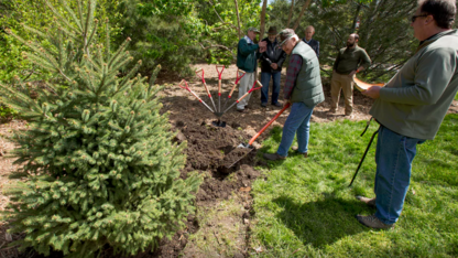 Bud Dasenbrock shovels dirt around the roots of the newly planted Engelmann spruce tree as other Arbor Day celebration participants look on.