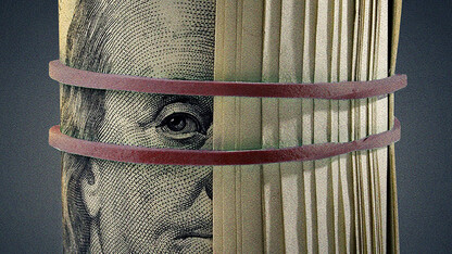 a bunch of $100 bills with Ben Franklin's face visible are rolled up and bound by a rubber band.