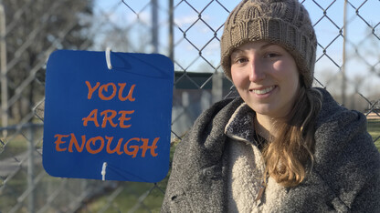 Taylor Schendt, a freshman honors student, stands next to the sign she made for a project in Nebraska's "Street Art: Art in the Urban Environment" course. The honors seminar was led by Sandra Williams, associate professor of art.