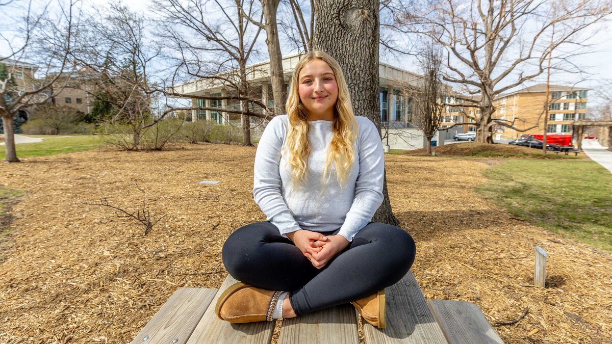 Hannah Haun sits in front of a tree in the East Campus Arboretum.