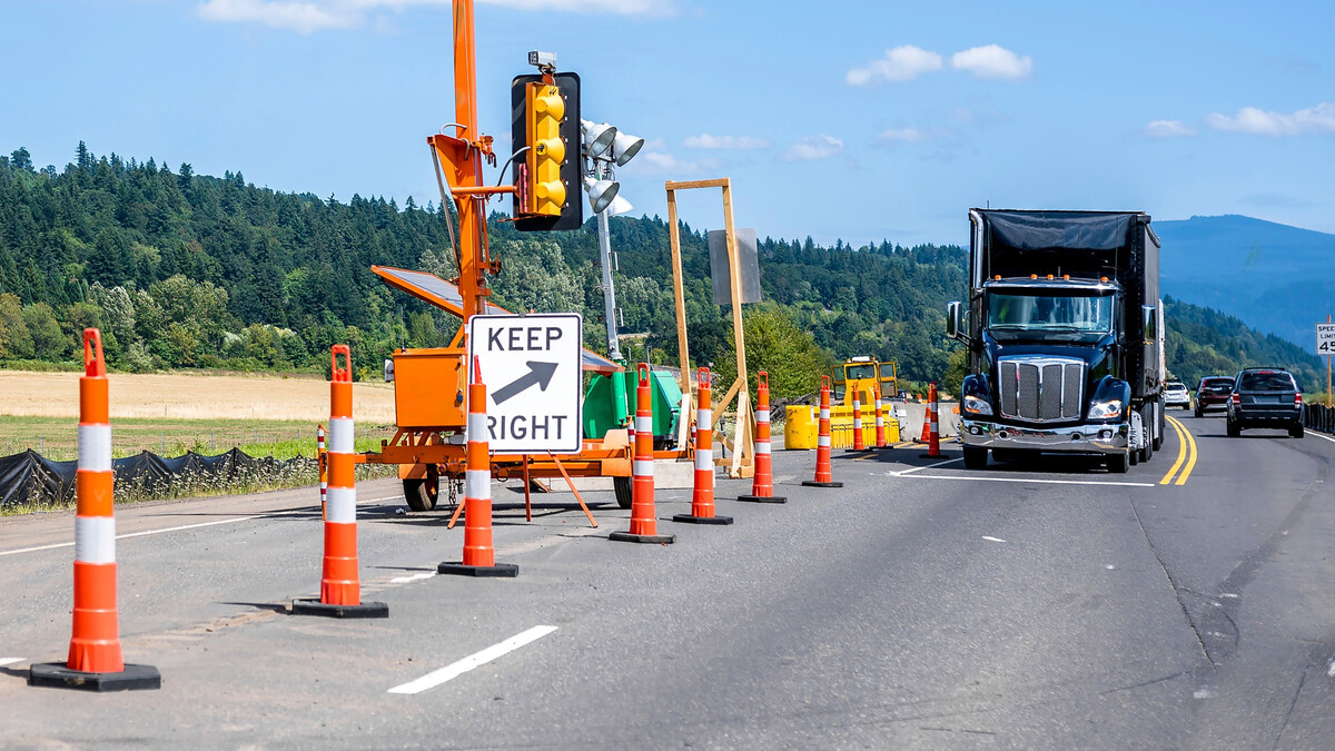 A black semi truck stops at a road work stop, with cones blocking off a lane.