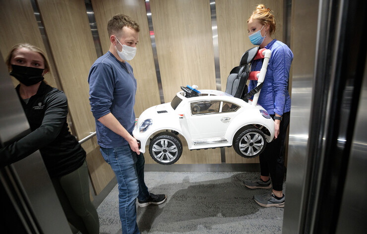 Ethan Bowles and Jamie Troester, a physical therapy student from UNMC, carry a completed electric car out of an elevator during the April 2 GoBabyGo! event.