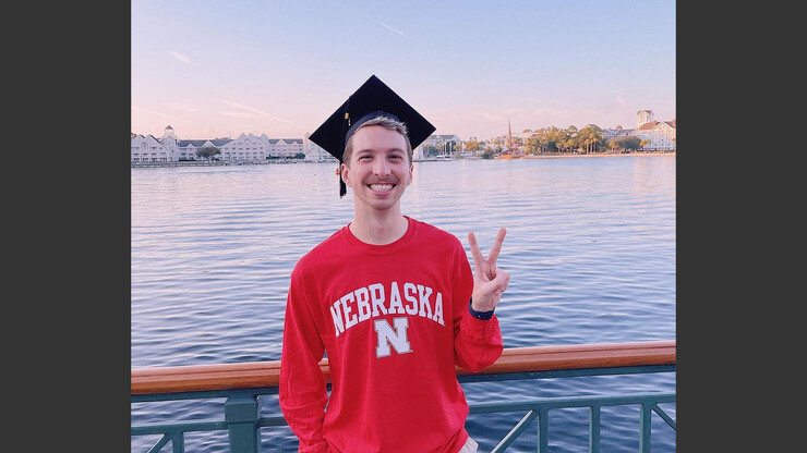 Husker graduate giving the peace symbol while wearing a mortar board.