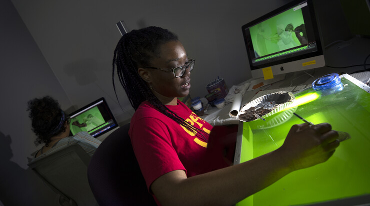 Imani Brown, a sophomore art student, paints over live-action scenes with an animation technique called rotoscoping. Brown, whose career goal is to create animated cartoons, is part of a team at Nebraska that is creating an animated film depicting the life of Ann “Anna” Williams, an enslaved woman who jumped out of a third-story window in Washington D.C. in 1815  after she had been sold into the cotton industry.  Another student animator, Thalia Rodgers, a senior art student, works on another part of the scene in the background.