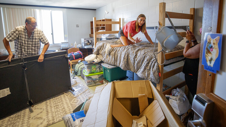 Kailey Trampe of Axtell, Nebraska, pauses for a quick smile as her mother, Sara, takes a photo. Her father, Todd, looks on as he assembles a futon during the university’s first day of student move-in to campus residence halls on Aug. 13.
