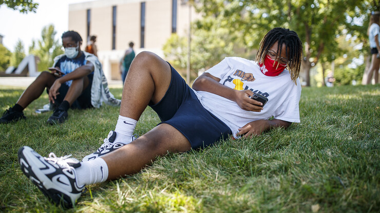 Da’Von George checks his phone while resting in the grass outside of the Woods Art Building before his photography class on the first day of the fall semester.